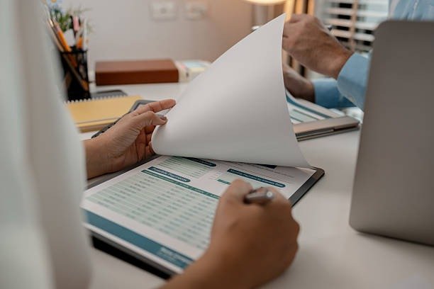 A person holds a paper and pen while working on a laptop, focused on professional credit counseling tasks.
